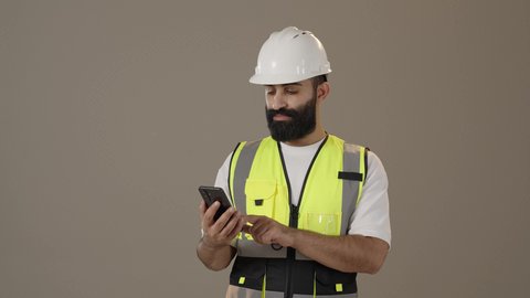 A Saudi Arabian Gulf engineer wearing a protective jacket and helmet holding a mobile phone, the development and growth of the engineering field in the Kingdom of Saudi Arabia, the integration of modern and advanced technologies into engineering work, working in the engineering sector