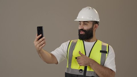 تطور و نمو مجال الهندسة في المملكة العربية السعودية, دمج التقنيات الحديثة و المتطورة بالأعمال الهندسية, العمل في القطاع الهندسي,مهندس عربي خليجي سعودي يرتدي سترة و خوذة الحماية يحمل بيديه الهاتف المحمول بايماءات الجوده والامتياز