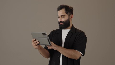 Chatting on a tablet, spending free time practicing hobbies, a portrait of a Saudi Arabian Gulf man wearing casual clothes holding a tablet in his hands, using technology in entertainment
