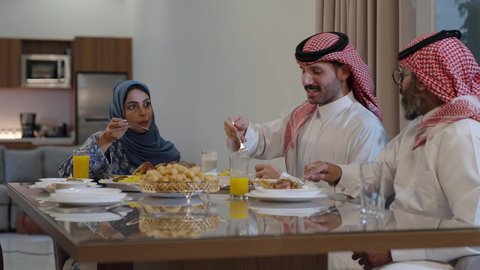 اجتماع الأسرة حول مائدة الطعام، افطار الصائم وقت أذان المغرب في رمضان، أجواء دينية رمضانية، عائلة عربية خليجية سعودية تجلس حول مائدة الطعام في المنزل، سفرة مليئة بالمأكولات الشهية