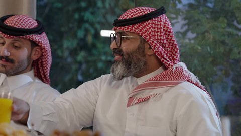 افطار الصائم وقت أذان المغرب في رمضان، أجواء دينية رمضانية، عائلة عربية خليجية سعودية تجلس حول مائدة الطعام في المنزل، سفرة مليئة بالمأكولات الشهية، اجتماع الأسرة حول مائدة الطعام