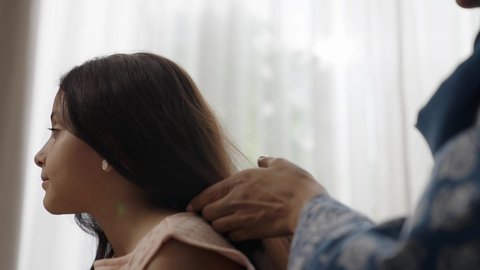  العناية والاهتمام بالأناقة والمظهر الخارجي، إيماءات السعادة والسرور، المحافظة على شعر صحي وأنيق، امراة عربية خليجية سعودية ترتدي العباءة والحجاب تجلس على الكنبة تقوم بتصفيف وتمشيط شعر ابنتها باستخدام الفرشاة ( المشط ) 