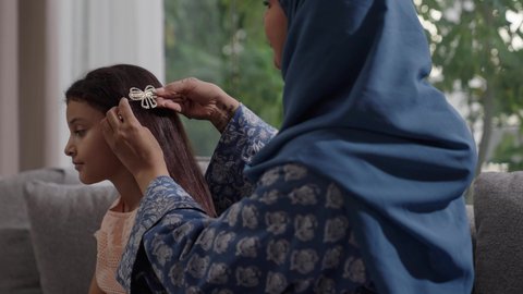  العناية والاهتمام بالأناقة والمظهر الخارجي، إيماءات السعادة والسرور، المحافظة على شعر صحي وأنيق، امراة عربية خليجية سعودية ترتدي العباءة والحجاب تجلس على الكنبة تقوم بتصفيف وتمشيط شعر ابنتها باستخدام الفرشاة ( المشط ) 