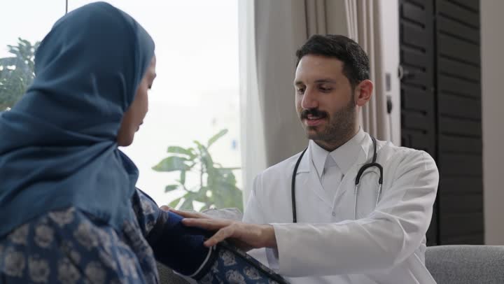 استخدام الميزان الالكتروني الحديث والمتطور للفحص المنزلي السريع,  طبيب عربي خليجي سعودي يرتدي المعطف الطبي يقوم بقياس ضغط الدم للمريضة في المنزل, مفهوم الرعاية الصحية والاهتمام بالصحة الجسدية