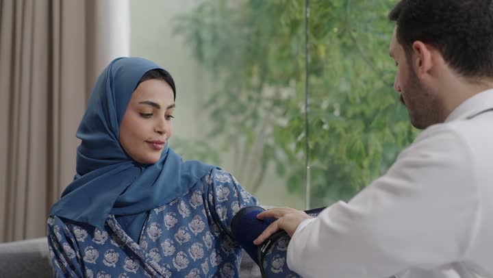 استخدام الميزان الالكتروني الحديث والمتطور للفحص المنزلي السريع,  طبيب عربي خليجي سعودي يرتدي المعطف الطبي يقوم بقياس ضغط الدم للمريضة في المنزل, مفهوم الرعاية الصحية والاهتمام بالصحة الجسدية