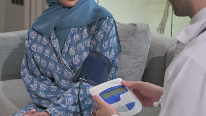 استخدام الميزان الالكتروني الحديث والمتطور للفحص المنزلي السريع,  طبيب عربي خليجي سعودي يرتدي المعطف الطبي يقوم بقياس ضغط الدم للمريضة في المنزل, مفهوم الرعاية الصحية والاهتمام بالصحة الجسدية