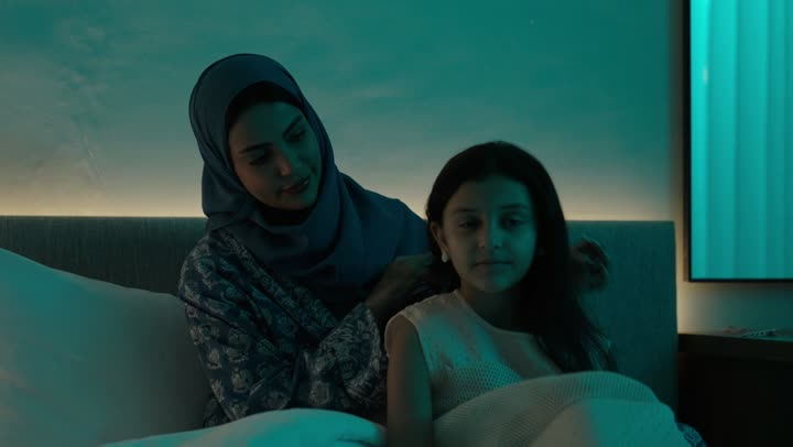 الاهتمام والعناية بالأناقة والمظهر الخارجي، إيماءات السعادة والسرور، المحافظة على شعر صحي وأنيق، امراة عربية خليجية سعودية ترتدي العباءة والحجاب تجلس على السرير تقوم بتصفيف وتمشيط شعر ابنتها باستخدام الفرشاة ( المشط )