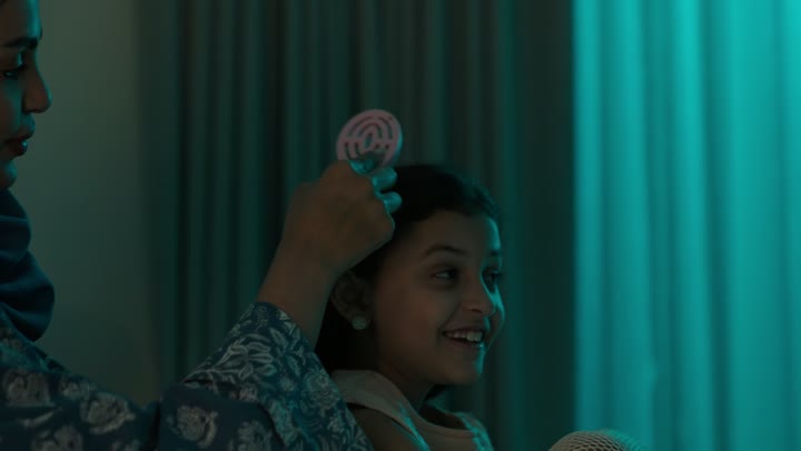 امراة عربية خليجية سعودية ترتدي العباءة والحجاب تجلس على السرير تقوم بتصفيف وتمشيط شعر ابنتها باستخدام الفرشاة ( المشط )، الاهتمام والعناية بالأناقة والمظهر الخارجي، إيماءات السعادة والسرور، المحافظة على شعر صحي وأنيق