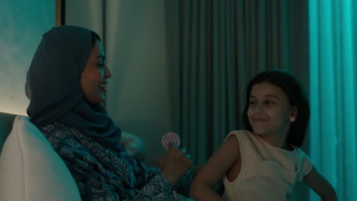 امراة عربية خليجية سعودية ترتدي العباءة والحجاب تجلس على السرير تقوم بتصفيف وتمشيط شعر ابنتها باستخدام الفرشاة ( المشط )، الاهتمام والعناية بالأناقة والمظهر الخارجي، إيماءات السعادة والسرور، المحافظة على شعر صحي وأنيق