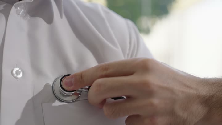 طبيب عربي خليجي سعودي يرتدي الثوب التقليدي يقوم بفحص رجل عبر سماعة الأذن في المنزل، استخدام سماعة الطبيب لسماع نبضات القلب، العمل في القطاع الصحي في السعودية،  القيام بالرعاية الصحية والاهتمام بصحة المرضى