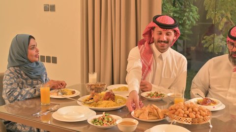 اجتماع الأسرة حول مائدة الإفطار المليئة بأصناف المأكولات والمقبلات الشهية، موعد كسر الصيام عند أذان المغرب في رمضان المبارك، فطور رمضاني عائلي، عائلة عربية خليجية سعودية تجلس بايماءات السرور، حسن الضيافة وإكرام الأخرين، أجواء عائلية روحانية دينية إسلامية