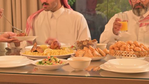  أجواء عائلية روحانية دينية إسلامية، اجتماع الأسرة حول مائدة الإفطار المليئة بأصناف المأكولات والمقبلات الشهية، موعد كسر الصيام عند أذان المغرب في رمضان المبارك، فطور رمضاني عائلي، عائلة عربية خليجية سعودية تجلس بايماءات السرور، حسن الضيافة وإكرام الأخرين