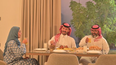  فطور رمضاني عائلي، عائلة عربية خليجية سعودية تجلس بايماءات السرور، حسن الضيافة وإكرام الأخرين, أجواء عائلية روحانية دينية إسلامية، اجتماع الأسرة حول مائدة الإفطار المليئة بأصناف المأكولات والمقبلات الشهية، موعد كسر الصيام عند أذان المغرب في رمضان المبارك