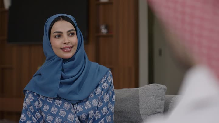 Serving authentic Arabic hot drinks on holidays, authentic Saudi customs and traditions on Islamic occasions, generous hospitality and warm welcome in Saudi Arabia, a smiling young Saudi Arabian Gulf woman wearing an abaya and hijab pouring Gulf coffee and serving it to guests in the living room