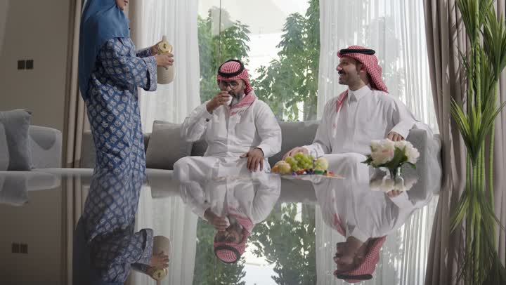 كرم الضيافة وحسن الاستقبال في السعودية, شابة عربية خليجية سعودية مبتسمة ترتدي العباءة والحجاب تقوم بصب القهوة الخليجية وتقديمها للضيوف في صالة المنزل، تقديم المشروبات الساخنة العربية الأصيلة في الأعياد، أصالة عادات وتقاليد المجتمع السعودي في المناسبات الاسلامية