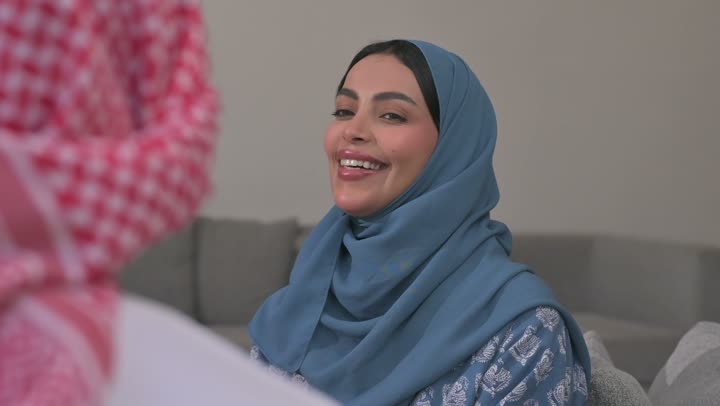 كرم الضيافة وحسن الاستقبال في السعودية, شابة عربية خليجية سعودية مبتسمة ترتدي العباءة والحجاب تقوم بصب القهوة الخليجية وتقديمها للضيوف في صالة المنزل، تقديم المشروبات الساخنة العربية الأصيلة في الأعياد، أصالة عادات وتقاليد المجتمع السعودي في المناسبات الاسلامية