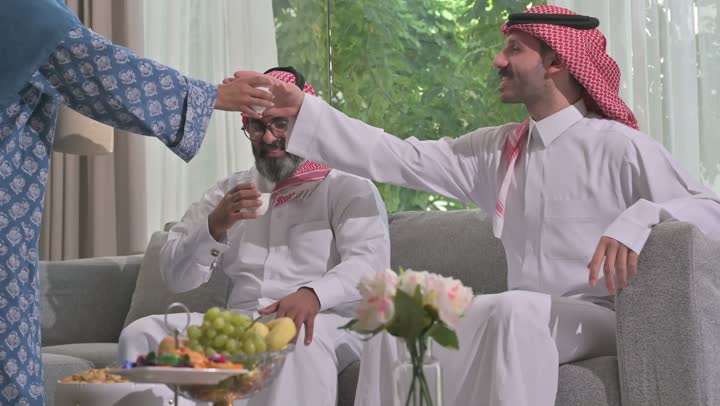 أصالة عادات وتقاليد المجتمع السعودي في المناسبات الاسلامية, كرم الضيافة وحسن الاستقبال في السعودية, شابة عربية خليجية سعودية مبتسمة ترتدي العباءة والحجاب تقوم بصب القهوة الخليجية وتقديمها للضيوف في صالة المنزل, تقديم المشروبات الساخنة العربية الأصيلة في الأعياد