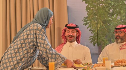 اجتماع الأسرة حول مائدة الإفطار المليئة بأصناف المأكولات والمقبلات الشهية، موعد كسر الصيام عند أذان المغرب في رمضان المبارك، فطور رمضاني عائلي، عائلة عربية خليجية سعودية تجلس بايماءات السرور، حسن الضيافة وإكرام الأخرين، أجواء عائلية روحانية دينية إسلامية