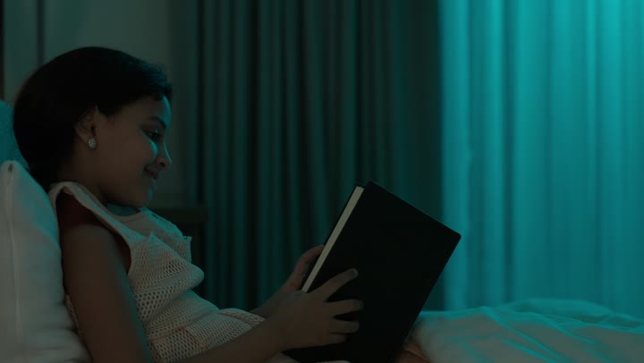 تمضية أوقات الفراغ بالتعلم والتثقف الذاتي, إيماءات الانتباه والتركيز بالمطالعة, تصوير مقرب لفتاة عربية خليجية سعودية تجلس على السرير تقوم بالقراءة بتمعن قبل النوم , مطالعة القصص التصويرية المسلية, تنمية مهارات القراءة للأطفال, الاهتمام بتصفح الكتب المفيدة