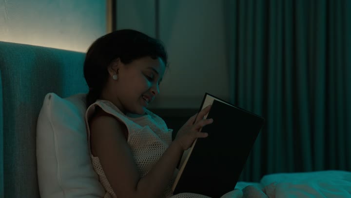 تمضية أوقات الفراغ بالتعلم والتثقف الذاتي, إيماءات الانتباه والتركيز بالمطالعة, تصوير مقرب لفتاة عربية خليجية سعودية تجلس على السرير تقوم بالقراءة بتمعن قبل النوم , مطالعة القصص التصويرية المسلية, تنمية مهارات القراءة للأطفال, الاهتمام بتصفح الكتب المفيدة