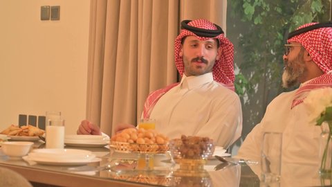 موعد كسر الصيام عند أذان المغرب في رمضان المبارك، فطور رمضاني عائلي، عائلة عربية خليجية سعودية تجلس بايماءا السرور، حسن الضيافة وإكرام الأخرين, أجواء عائلية روحانية دينية إسلامية، اجتماع الأسرة حول مائدة الإفطار المليئة بأصناف المأكولات والمقبلات الشهية