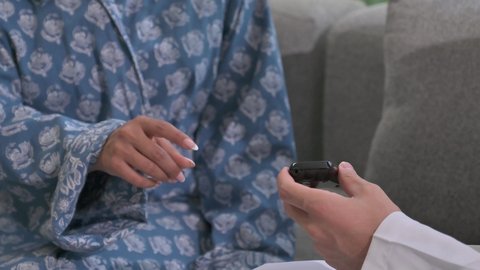 المتابعة الدورية لمرضى داء السكري, الفحوصات الطبية السريعة لمعرفة نسبة السكر في الدم، استخدام الأجهزة الالكترونية للتحاليل المنزلية، شابة سعودية مصابة بحالة مرضية مزمنة, تصوير مقرب لرجل عربي خليجي سعودي يرتدي الثوب التقليدي يقوم بوخز اصبع امرأة