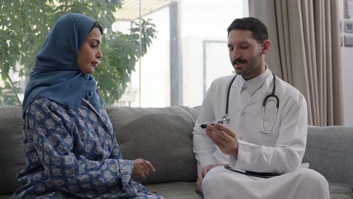 شابة سعودية مصابة بحالة مرضية مزمنة, المتابعة الدورية لمرضى داء السكري, الفحوصات الطبية السريعة لمعرفة نسبة السكر في الدم، استخدام الأجهزة الالكترونية للتحاليل المنزلية، تصوير مقرب لطبيب عربي خليجي سعودي يرتدي المعطف الابيض وسماعة الأذن يقوم بوخز اصبع امرأة