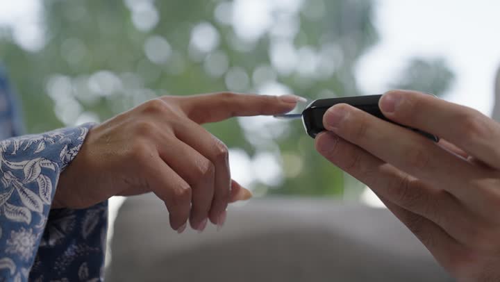 شابة سعودية مصابة بحالة مرضية مزمنة, المتابعة الدورية لمرضى داء السكري, الفحوصات الطبية السريعة لمعرفة نسبة السكر في الدم، استخدام الأجهزة الالكترونية للتحاليل المنزلية، تصوير مقرب لطبيب عربي خليجي سعودي يرتدي المعطف الابيض وسماعة الأذن يقوم بوخز اصبع امرأة