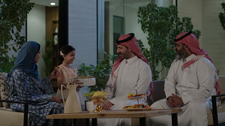 صلة الرحم والترابط الاسري, فرحة وبهجة الابناء في ايام العيد السعيد, التجمعات والزيارات الاسرية في الأعياد والمناسبات الاسلامية, رجل عربي خليجي سعودي يرتدي الزي التقليدي يجلس مع أحفاده بإيماءات الفرح والسرور، ضيافة وحلوى العيد، حسن استقبال وإكرام الضيف