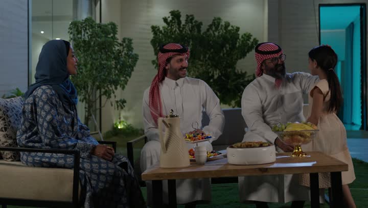 صلة الرحم والترابط الاسري, فرحة وبهجة الابناء في ايام العيد السعيد, التجمعات والزيارات الاسرية في الأعياد والمناسبات الاسلامية, رجل عربي خليجي سعودي يرتدي الزي التقليدي يجلس مع أحفاده بإيماءات الفرح والسرور، ضيافة وحلوى العيد، حسن استقبال وإكرام الضيف