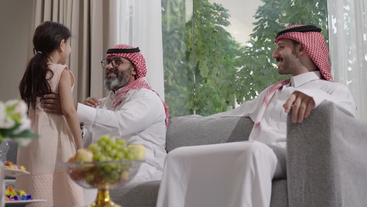 صلة الرحم والترابط الاسري, فرحة وبهجة الابناء في ايام العيد السعيد, التجمعات والزيارات الاسرية في الأعياد والمناسبات الاسلامية, رجل عربي خليجي سعودي يرتدي الزي التقليدي يجلس مع أحفاده بإيماءات الفرح والسرور، ضيافة وحلوى العيد، حسن استقبال وإكرام الضيف