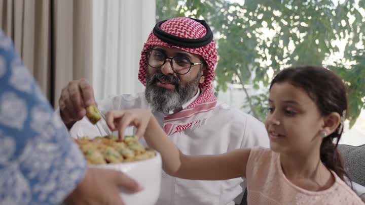 صلة الرحم والترابط الاسري, فرحة وبهجة الابناء في ايام العيد السعيد, التجمعات والزيارات الاسرية في الأعياد والمناسبات الاسلامية, رجل عربي خليجي سعودي يرتدي الزي التقليدي يجلس مع أحفاده بإيماءات الفرح والسرور، ضيافة وحلوى العيد، حسن استقبال وإكرام الضيف