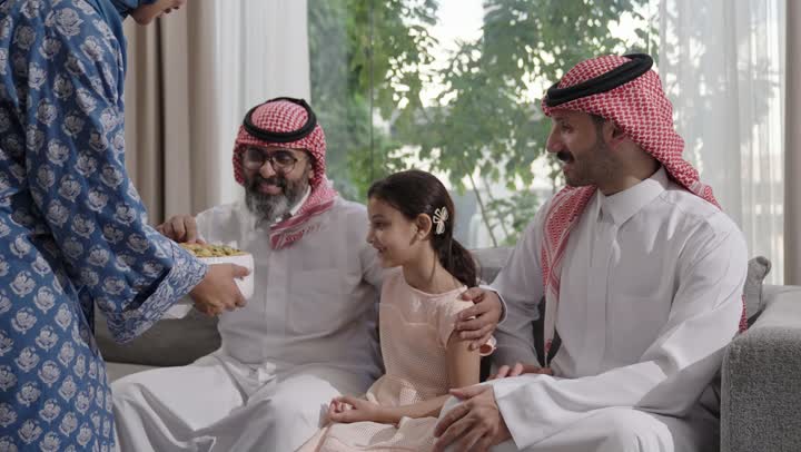 صلة الرحم والترابط الاسري, فرحة وبهجة الابناء في ايام العيد السعيد, التجمعات والزيارات الاسرية في الأعياد والمناسبات الاسلامية, رجل عربي خليجي سعودي يرتدي الزي التقليدي يجلس مع أحفاده بإيماءات الفرح والسرور، ضيافة وحلوى العيد، حسن استقبال وإكرام الضيف