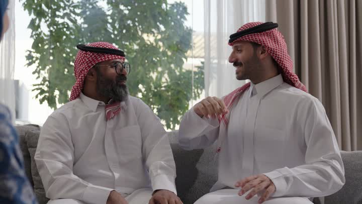 صلة الرحم والترابط الاسري, فرحة وبهجة الابناء في ايام العيد السعيد, التجمعات والزيارات الاسرية في الأعياد والمناسبات الاسلامية, رجل عربي خليجي سعودي يرتدي الزي التقليدي يجلس مع أحفاده بإيماءات الفرح والسرور، ضيافة وحلوى العيد، حسن استقبال وإكرام الضيف