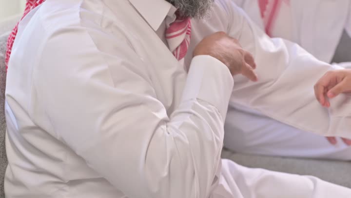 تقديم العيدية في العيد، مفهوم الحب والحنان، دور الأب في حياه الأبناء، تصوير مقرب لأب عربي خليجي سعودي يرتدي الثوب التقليدي والشماغ يجلس على كرسي يحتضن ابنته بين ذراعيه، قضاء وقت ممتع ومسلي، ايماءات السعادة والسرور،  اجواء اسرية مليئة بالفرح