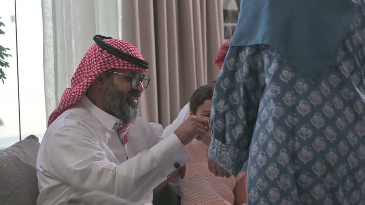 ضيافة وحلوى العيد، حسن استقبال وإكرام الضيف، صلة الرحم والترابط الاسري, فرحة وبهجة الابناء في ايام العيد السعيد, التجمعات والزيارات الاسرية في الأعياد والمناسبات الاسلامية, رجل عربي خليجي سعودي يرتدي الثوب التقليدي يجلس مع أحفاده بإيماءات الفرح والسرور