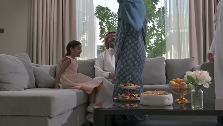 ضيافة وحلوى العيد، حسن استقبال وإكرام الضيف، صلة الرحم والترابط الاسري, فرحة وبهجة الابناء في ايام العيد السعيد, التجمعات والزيارات الاسرية في الأعياد والمناسبات الاسلامية, رجل عربي خليجي سعودي يرتدي الثوب التقليدي يجلس مع أحفاده بإيماءات الفرح والسرور