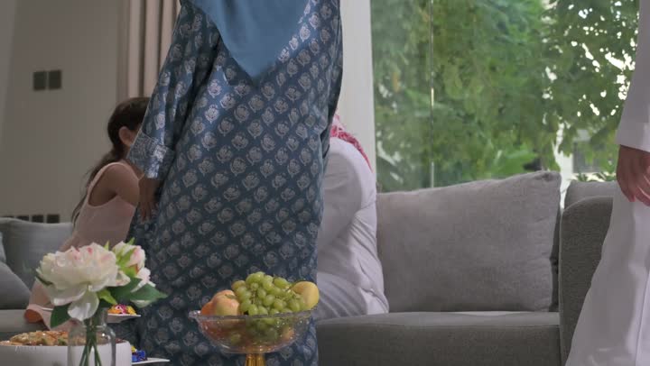 ضيافة وحلوى العيد، حسن استقبال وإكرام الضيف، صلة الرحم والترابط الاسري, فرحة وبهجة الابناء في ايام العيد السعيد, التجمعات والزيارات الاسرية في الأعياد والمناسبات الاسلامية, رجل عربي خليجي سعودي يرتدي الثوب التقليدي يجلس مع أحفاده بإيماءات الفرح والسرور