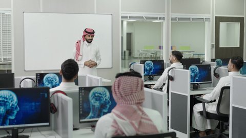 العلم والتعليم في المجتمع السعودي, إقامة دورات تدريبية للطلاب, متحدث ودكتور جامعي عربي خليجي سعودي يرتدي الشماغ والثوب التقليدي يقوم بإلقاء محاضرة أمام الطلبة, محاضرات ودورات تعليمية في السعودية، قاعة دراسية مجهزة بشاشات وأجهزة تقنية حديثة