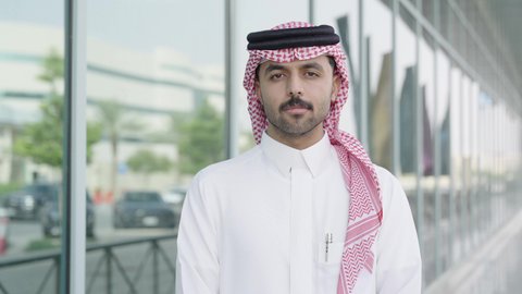 الاهتمام بالمظهر الخارجي، مفهوم الأناقة والوسامة، رجل عربي خليجي سعودي يرتدي الثوب والشماغ التقليدي ينظر إلى الكاميرا بإيماءات السرور، الوقوف بأيدي متقاطعة