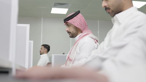 استخدام جهاز الحاسوب، التعليم العالي في الجامعات والكليات الأكاديمية, دمج التعلم مع التكنولوجيا، إجراء اختبارات وأبحاث العلمية، طلاب عرب خليجيون سعوديون يرتدون الزي التقليدي يقومون بحضور محاضرة في قاعة دراسية، جودة التعليم الجامعي في المملكة العربية السعودية