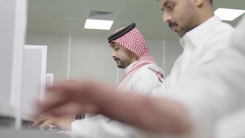 Integrating learning with technology, higher education in universities and academic colleges, conducting tests and scientific research online, Arab Gulf students from Saudi Arabia wearing traditional attire using a computer in a classroom, the quality of university education in the Kingdom of Saudi Arabia.