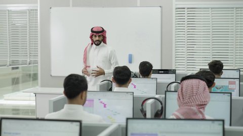 قاعة دراسية مجهزة بشاشات وأجهزة تقنية حديثة، العلم والتعليم في المجتمع السعودي, إقامة دورات تدريبية للطلاب, متحدث ودكتور جامعي عربي خليجي سعودي يرتدي الشماغ والثوب التقليدي يقوم بإلقاء محاضرة أمام الطلبة, محاضرات ودورات تعليمية في السعودية
