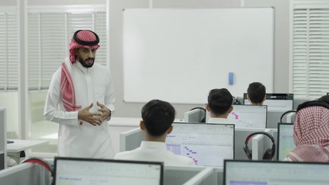 قاعة دراسية مجهزة بشاشات وأجهزة تقنية حديثة، العلم والتعليم في المجتمع السعودي, إقامة دورات تدريبية للطلاب, متحدث ودكتور جامعي عربي خليجي سعودي يرتدي الشماغ والثوب التقليدي يقوم بإلقاء محاضرة أمام الطلبة, محاضرات ودورات تعليمية في السعودية