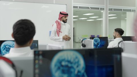 إقامة دورات تدريبية للطلاب, متحدث ودكتور جامعي عربي خليجي سعودي يرتدي الشماغ والثوب التقليدي يقوم بإلقاء محاضرة أمام الطلبة, العلم والتعليم في المجتمع السعودي, محاضرات ودورات تعليمية في السعودية، قاعة دراسية مجهزة بشاشات وأجهزة تقنية حديثة