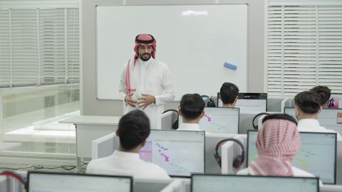 قاعة دراسية مجهزة بشاشات وأجهزة تقنية حديثة، العلم والتعليم في المجتمع السعودي, إقامة دورات تدريبية للطلاب, متحدث ودكتور جامعي عربي خليجي سعودي يرتدي الشماغ والثوب التقليدي يقوم بإلقاء محاضرة أمام الطلبة, محاضرات ودورات تعليمية في السعودية