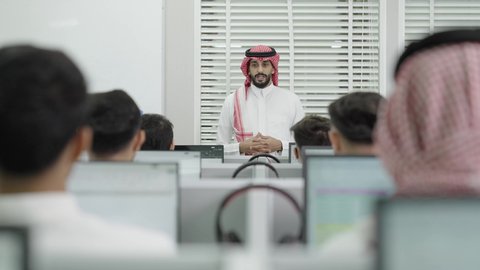 استخدام سماعات الرأس، قاعة دراسية مجهزة بشاشات وأجهزة تقنية حديثة، العلم والتعليم في المجتمع السعودي, إقامة دورات تدريبية للطلاب, متحدث ودكتور جامعي عربي خليجي سعودي يرتدي الشماغ والثوب التقليدي يقوم بإلقاء محاضرة أمام الطلبة, محاضرات ودورات تعليمية في السعودية