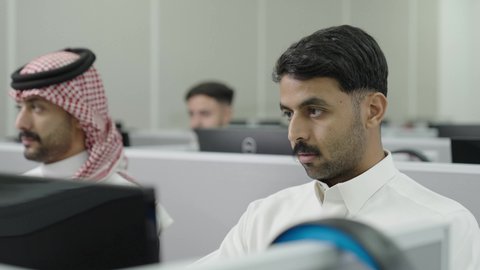 استخدام جهاز الحاسوب، التعليم العالي في الجامعات والكليات الأكاديمية, دمج التعلم مع التكنولوجيا، إجراء اختبارات وأبحاث العلمية، طلاب عرب خليجيون سعوديون يرتدون الزي التقليدي يقومون بحضور محاضرة في قاعة دراسية، جودة التعليم الجامعي في المملكة العربية السعودية