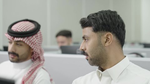 إيماءات التركيز والاندماج، دمج التعلم مع التكنولوجيا، التعليم العالي في الجامعات والكليات الأكاديمية, إجراء اختبارات وأبحاث علمية عبر الانترنت، طلاب عرب خليجيون سعوديون يرتدون الزي التقليدي يقومون باستخدام الحاسوب في قاعة دراسية، جودة التعليم الجامعي في المملكة