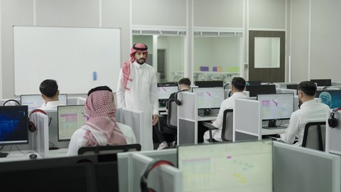 إقامة دورات تدريبية للطلاب, متحدث ودكتور جامعي عربي خليجي سعودي يرتدي الشماغ والثوب التقليدي يقوم بإلقاء محاضرة أمام الطلبة, العلم والتعليم في المجتمع السعودي, محاضرات ودورات تعليمية في السعودية، قاعة دراسية مجهزة بشاشات وأجهزة تقنية حديثة